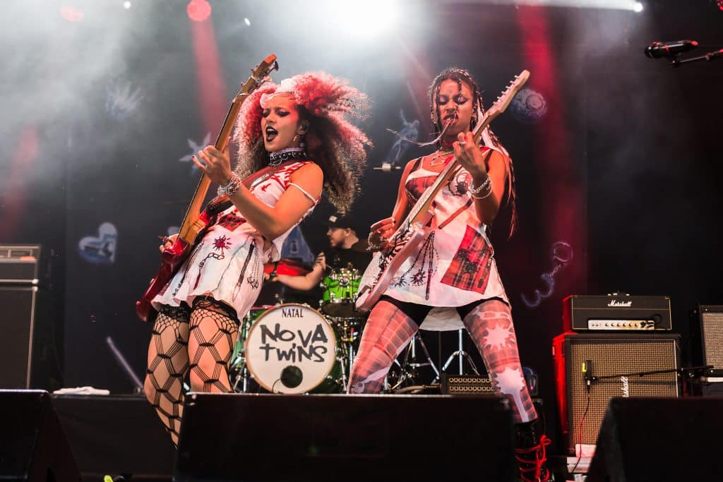 Amy Love and Georgia South of the band Nova Twins performing on stage, both with guitars, wearing punk-style clothing.