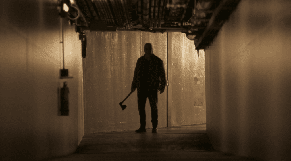 In a dimly lit hallway, a masked man wielding an ax stands, waiting to attack.