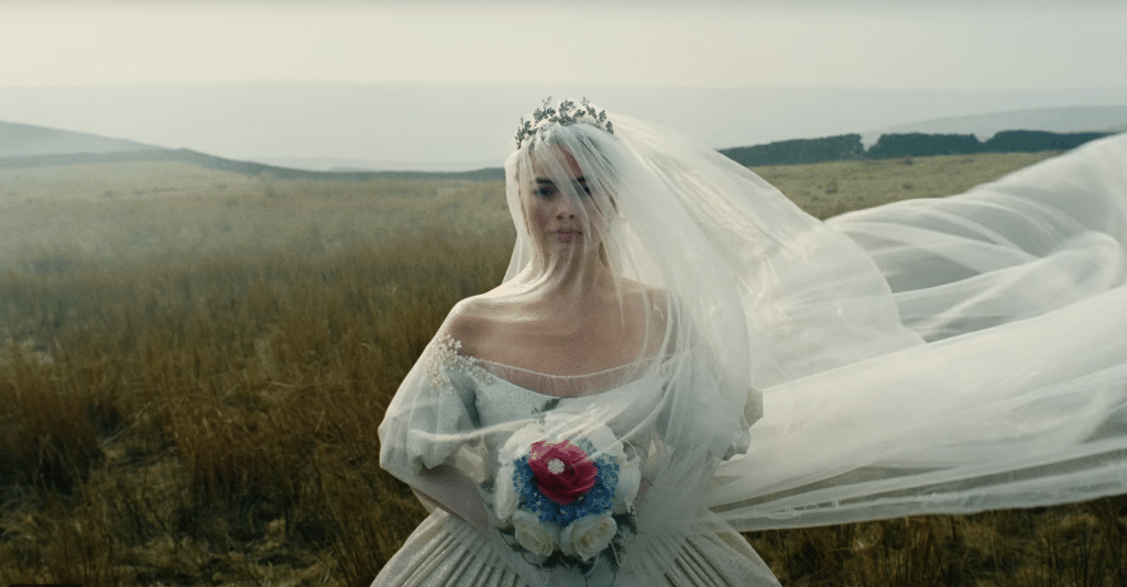 Catherine wears a flowing white wedding dress and holds a bouquet of flowers.