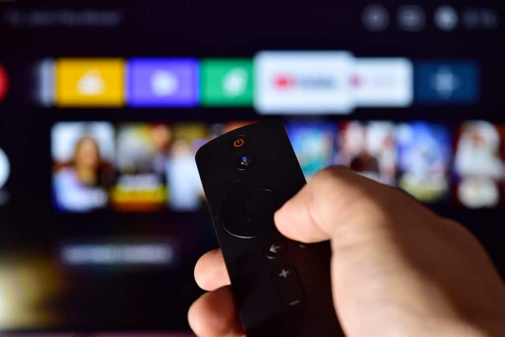 Hand holding a remote in front of TV full of streaming services.