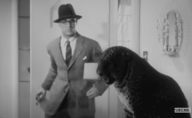A man in a suit and hat sees a leopard sitting in a bathroom.