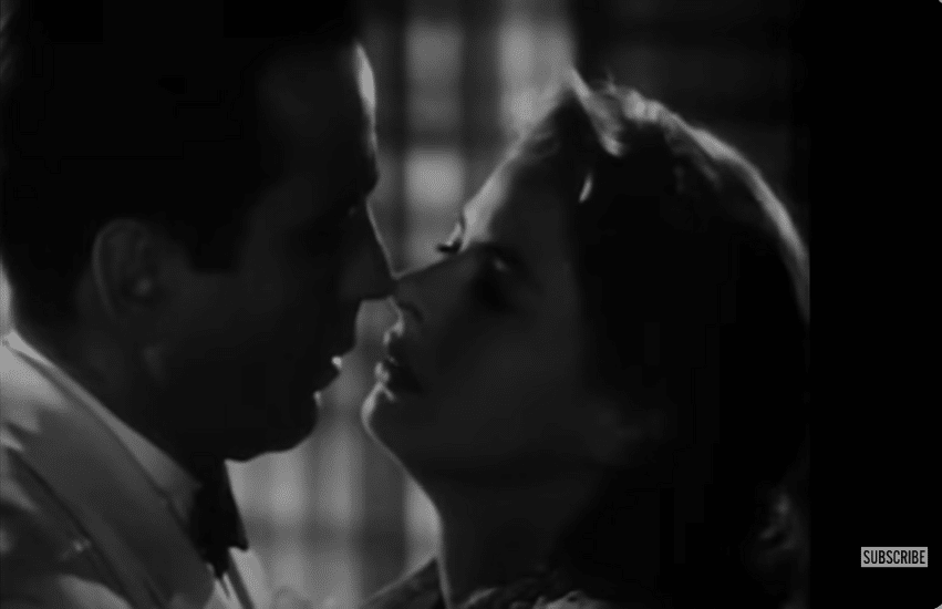 A man and a woman in close proximity stare at each other in a dark room.