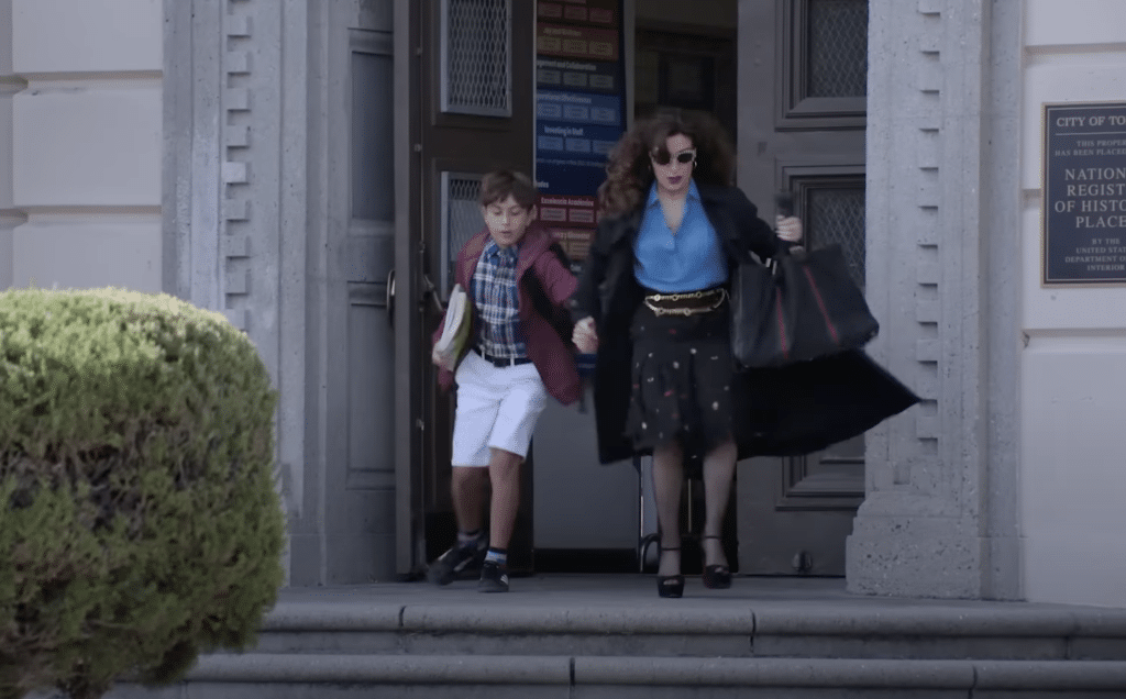 Esmeralda rushes to take her son out of school in 'The Paper.'