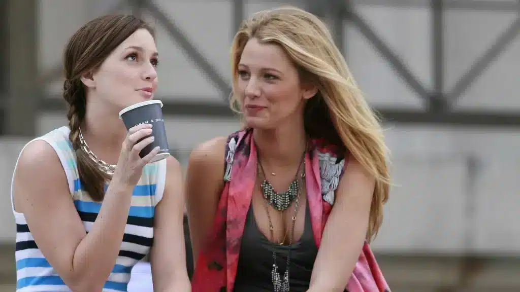 Gossip girl scene in which Blair Waldorf and Serena Van der Woodsen are sitting. Blair is drinking coffee. Serena is looking at her.