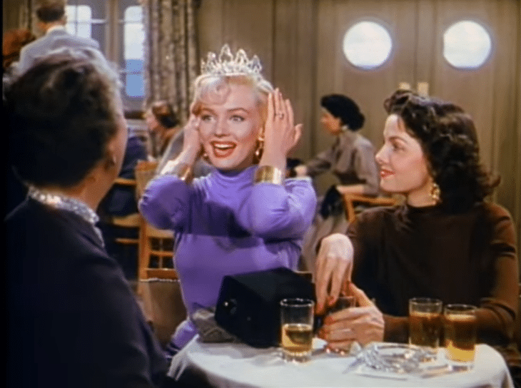 Marylin Monroe tries on a tiara and shows it to the few women surrounding her.