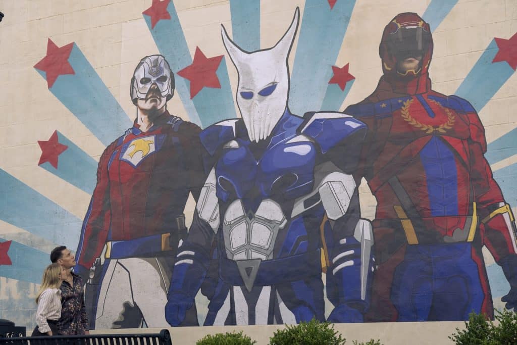 Smith (Cena) and Harcourt (Holland) looking up at a mural of "The Top Trio" from the parallel dimension.