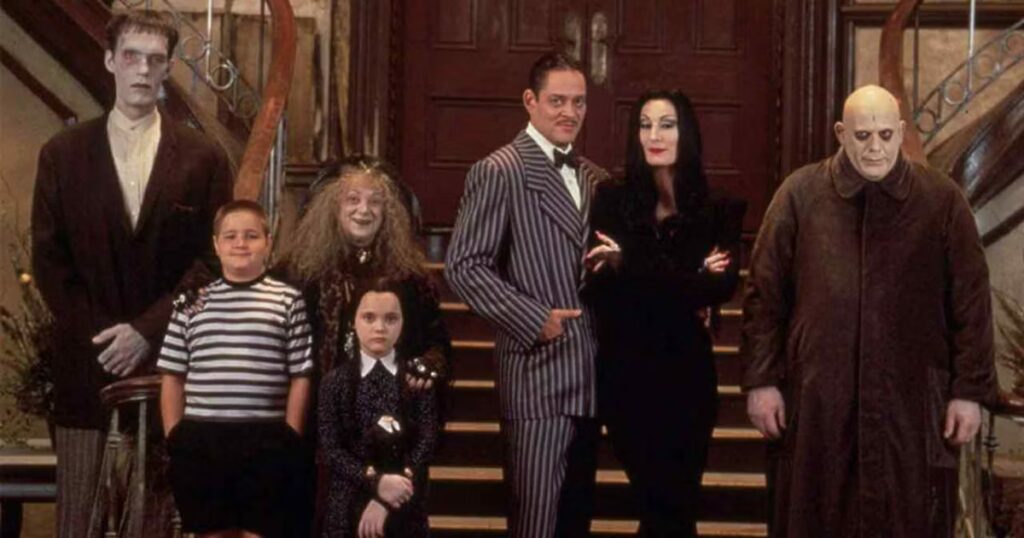 cast of the addams family stands tall in front of giant staircase
