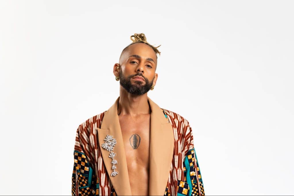 Image of a confident-looking black man with a great sense of style whose center chest is exposed to show a tattoo.