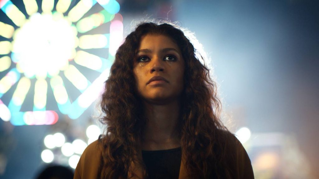 Zendaya looks up with a ferris wheel in the background.