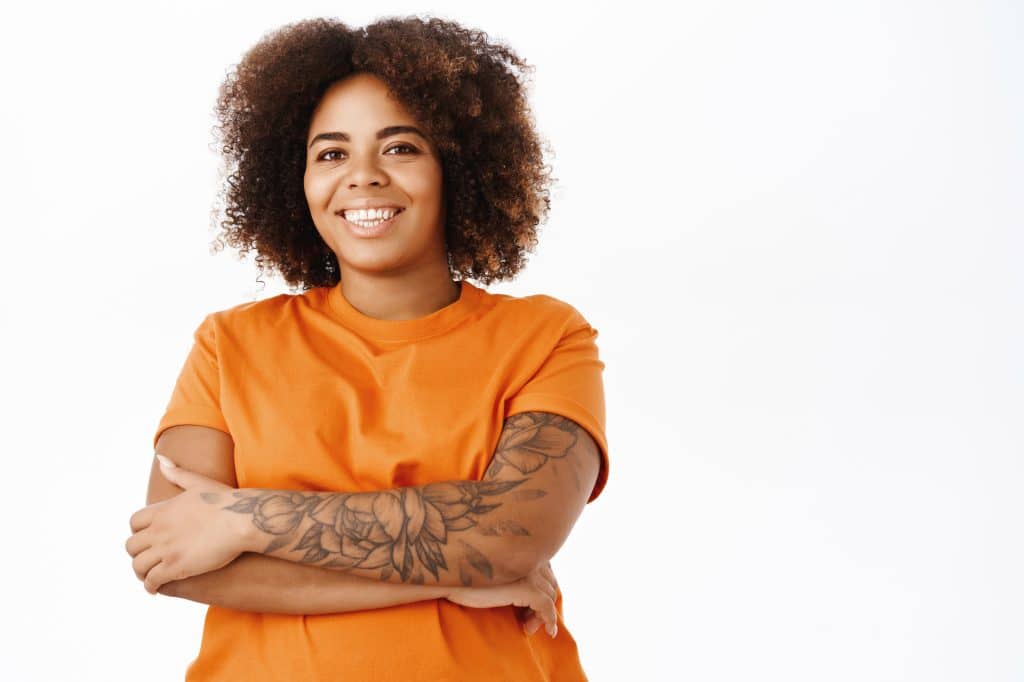 Image of a smiling young black woman with most of one arm covered in floral tattoos. She looks very happy.