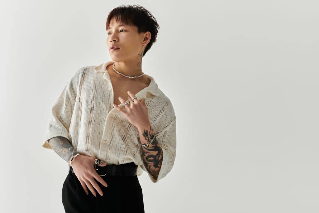 Image of an ethnically ambiguous young man who appears to be of Asian heritage who has most of both arms covered in tattoos as well as some on the side of his neck.