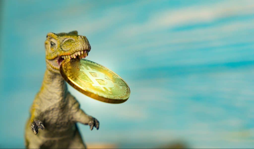 Toy t-rex with a bitcoin in its mouth, against a blue background.
