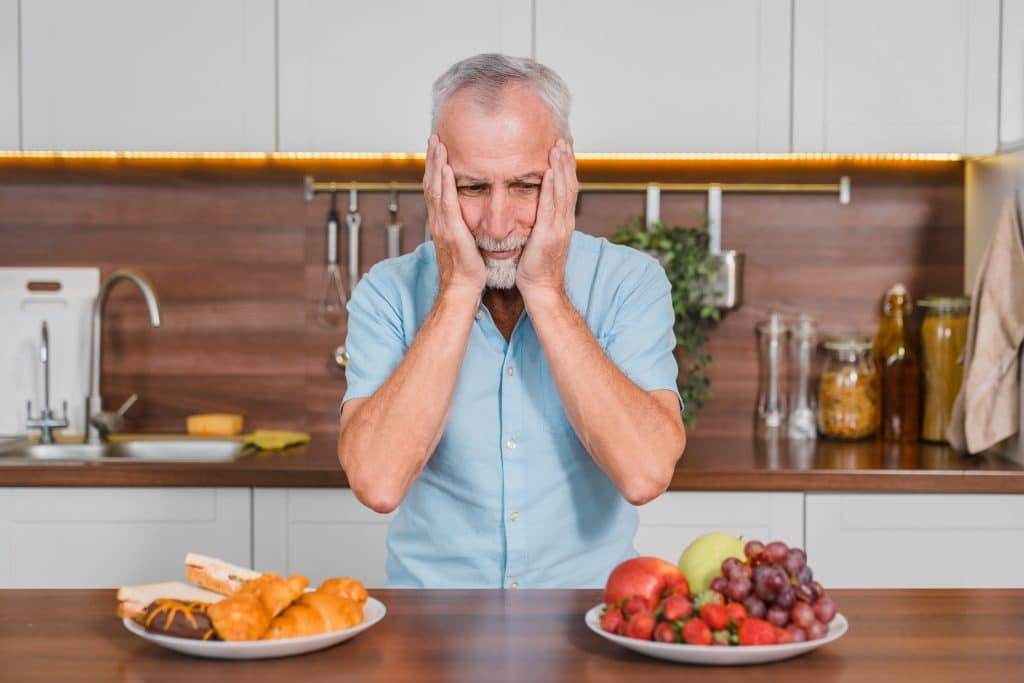 A man gazed at a plate of bread and a plate of fruit on the table, troubled over which to choose.