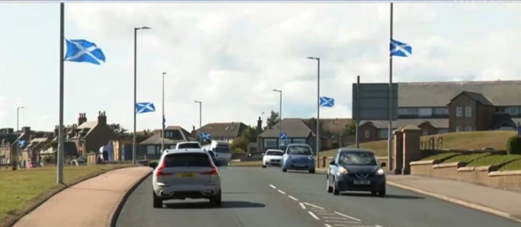 Scottish flags hung up on multiple lamp posts on a busy street.