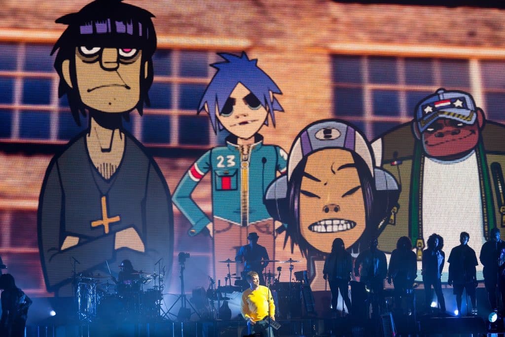People perform on a stage with a backdrop of animated versions of them.