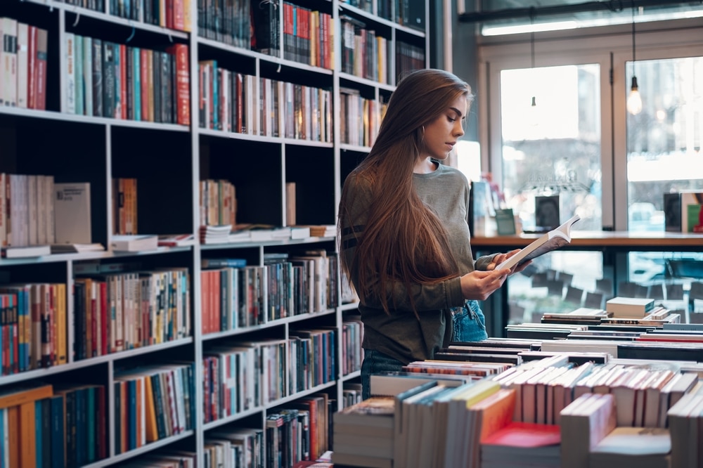 A female in a book shop, reading the blurb of a book
