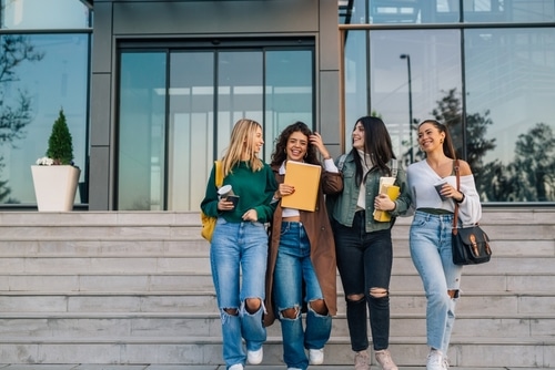 Four college girls walking down some steps outside a building. They are laughing and smiling.
