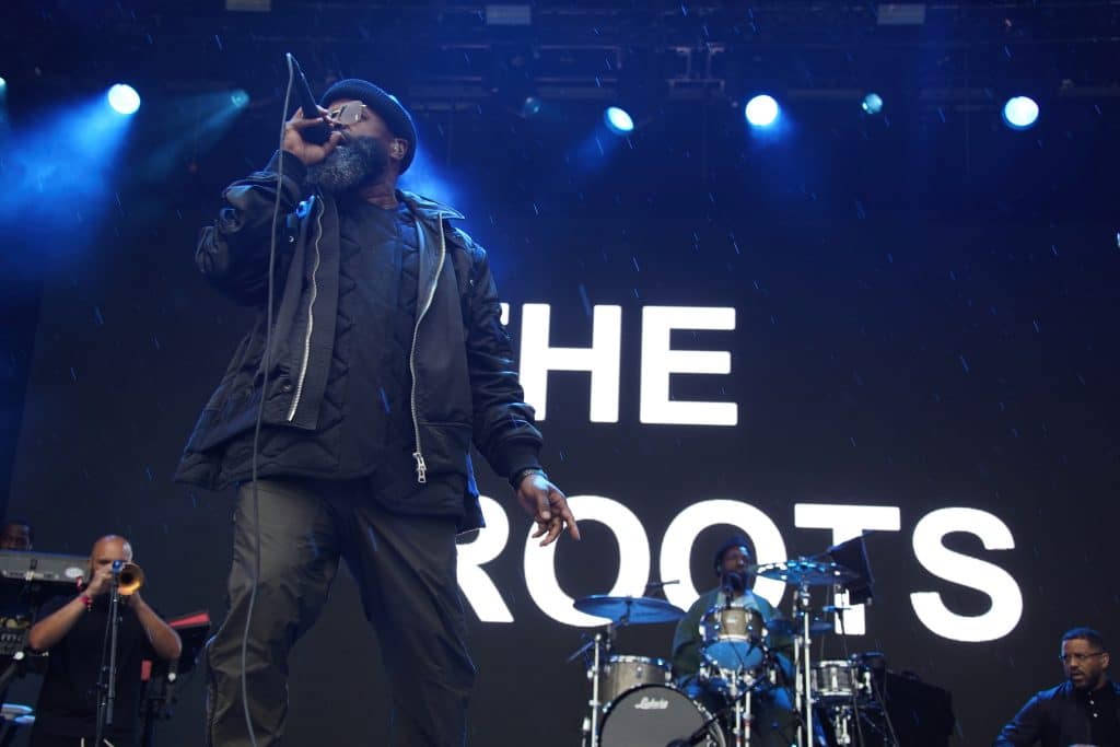 A man sings into a microphone with a band behind him.