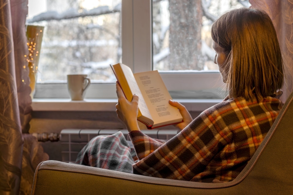 A woman reading a book in an armchair by a window