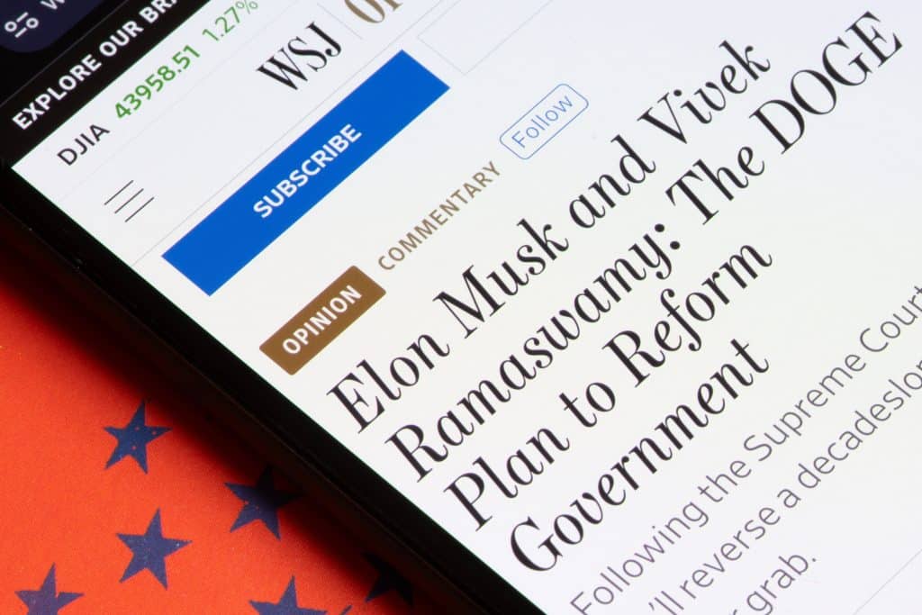 Image of a phone with a news headline on the screen reading "Elon Musk and Vivek Ramaswamy: The DOGE Plan to Reform Government"
