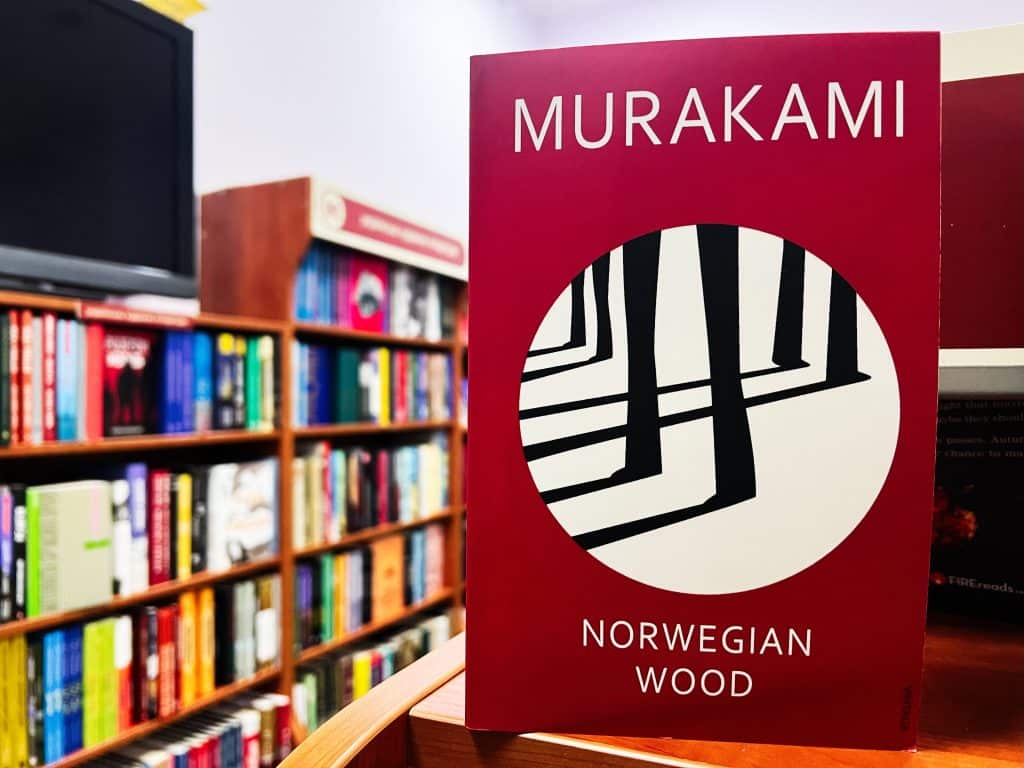 A propped up copy of Murakami's Norwegian Wood. The background consists of bookshelves.
