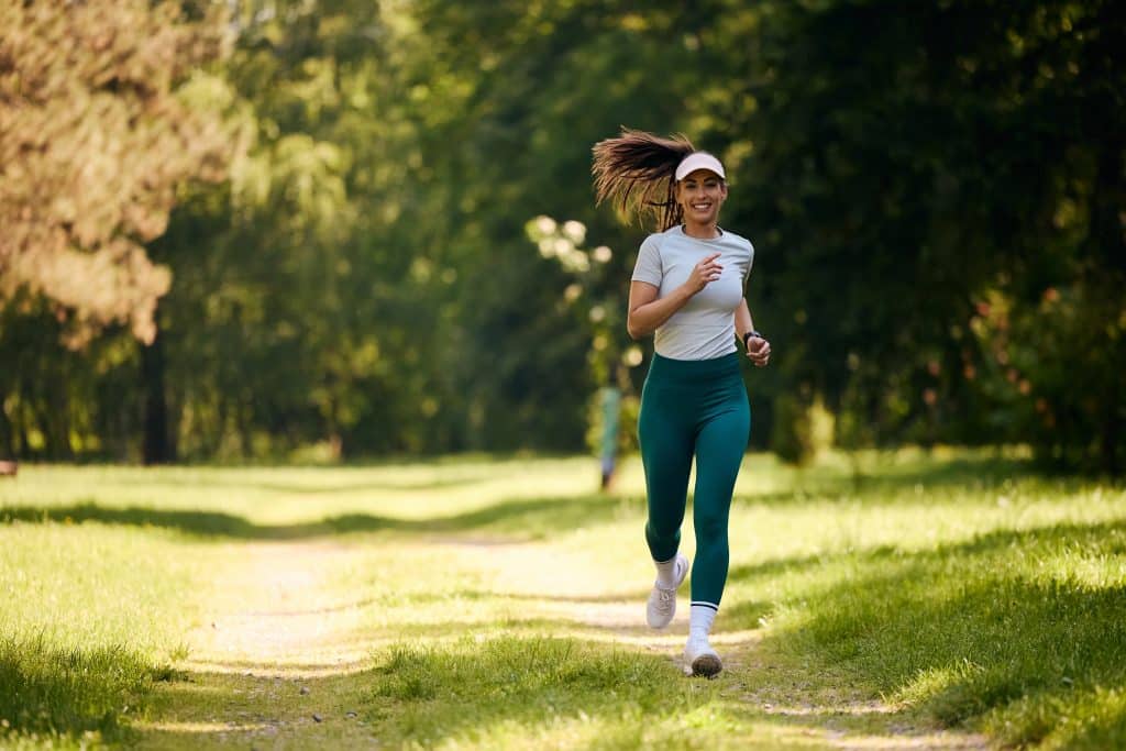 A lady running, engaged in aerobic exercise, against a backdrop of green woodland.