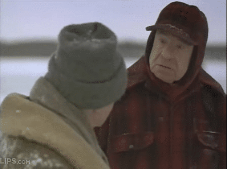 Two men wearing warm winter clothes talking to each other out in the snow