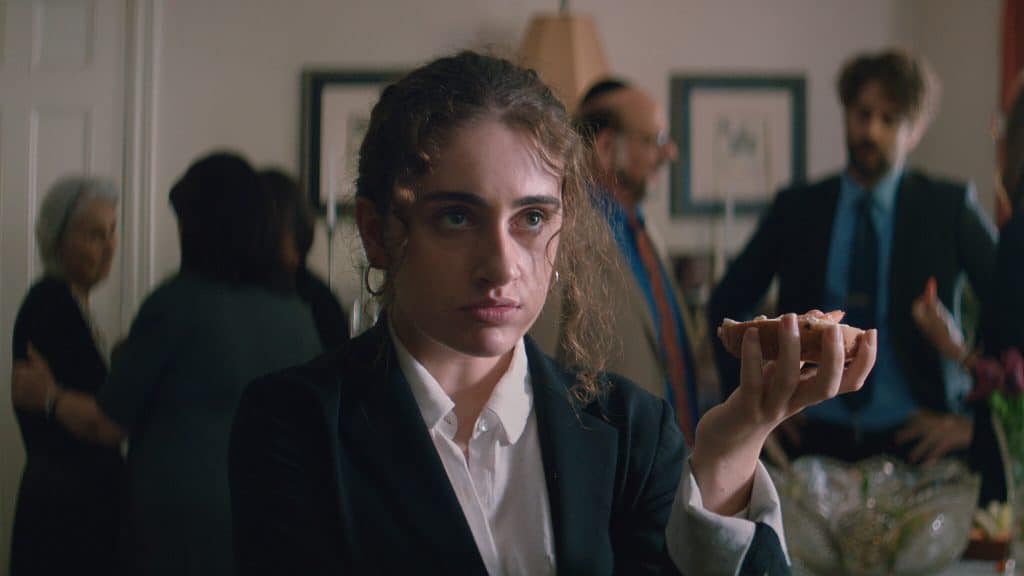 Rachel Sennott's character Danielle in Shiva baby holding a bagel in still shot.