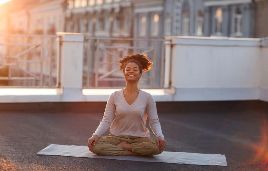 Cropped photo of a woman sitting in lotus pose on a mat and practicing yoga, a female doing the namaste gesture while meditating outdoors. Meditation and the mindfulness concept