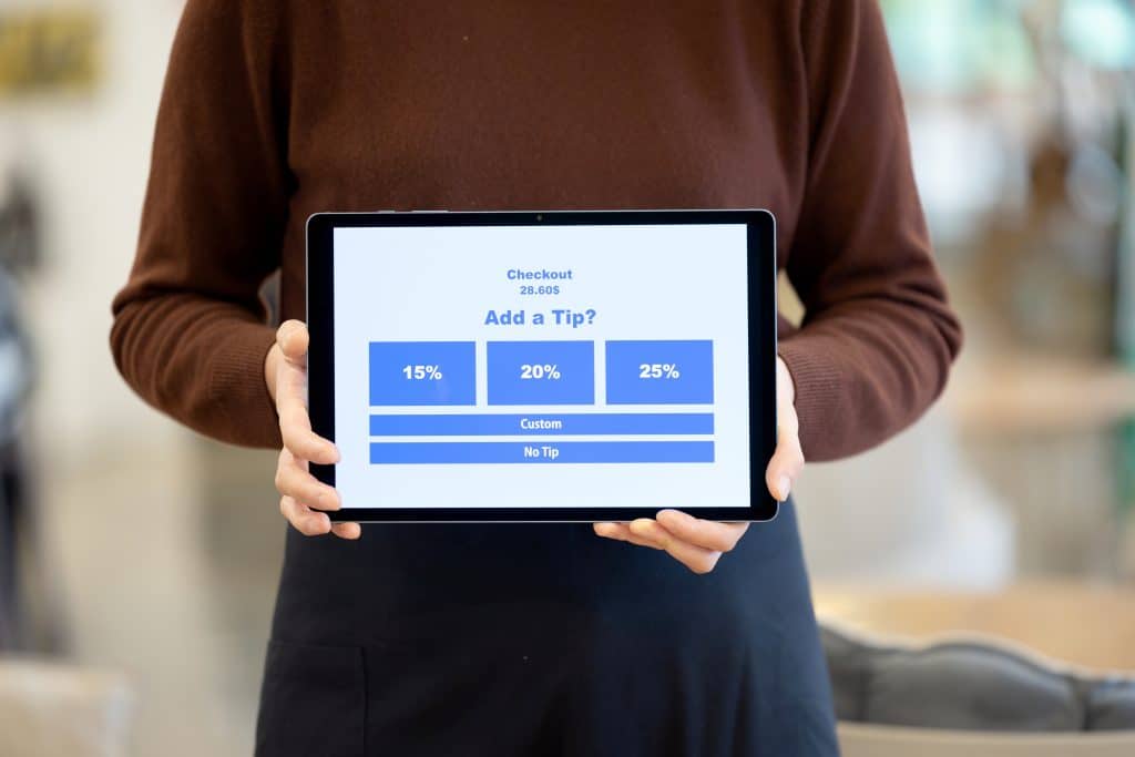 A person holding up a screen asking for a tip; an example of tip culture.