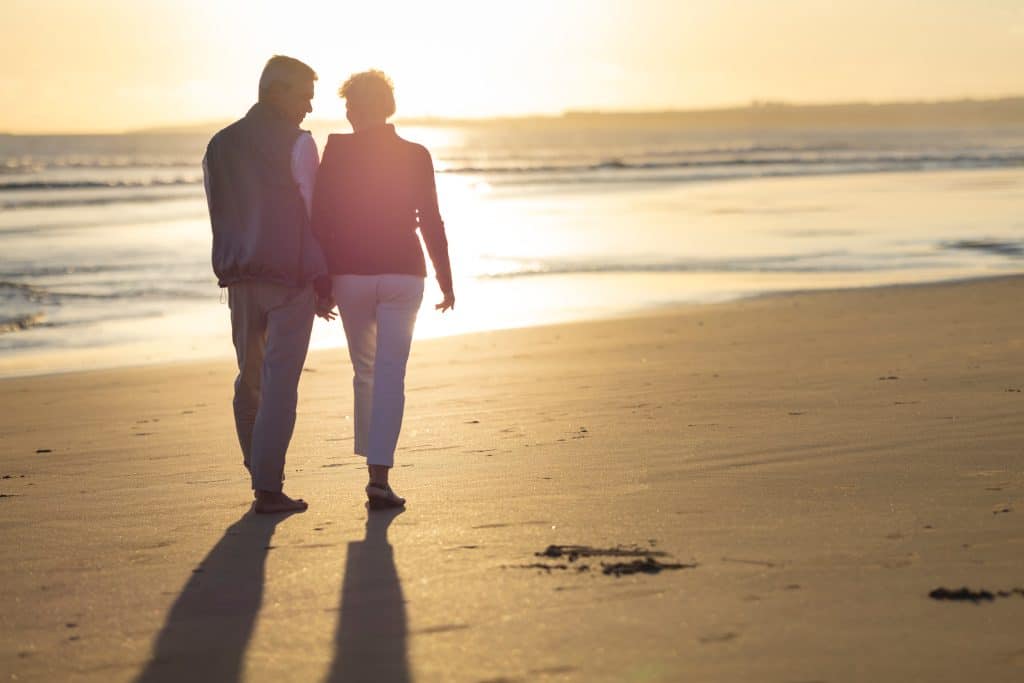 Senior couple walking on the beach at sunset holding hands