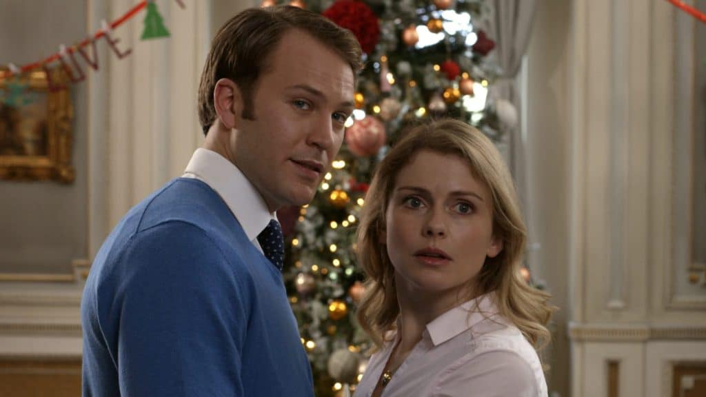 Amber and king Richard standing face to face looking worriedly out past the camera with a Christmas tree behind them.