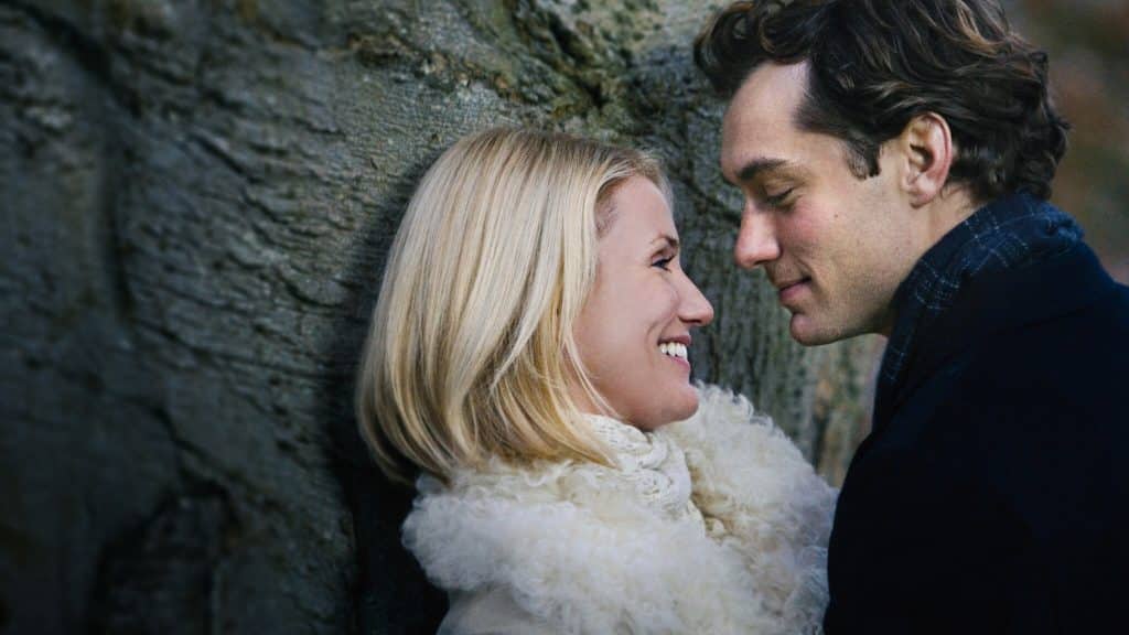 Two people looking into each others eyes as they hug, pushed up against a tree.