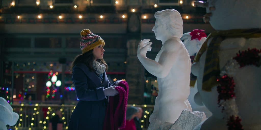 Kathy looking at her snowman holding a pink scarf.