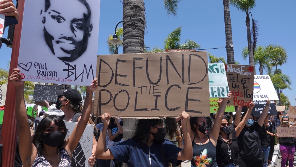 People hold signs during peaceful Black Lives Matter protest march, one of many in San Diego County, California in 2020. One sign reads "Defund Police".