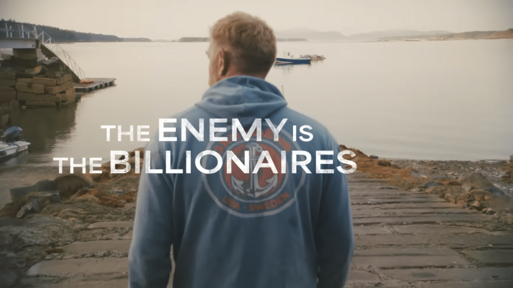Graham Platner in his Senate campaign video, and the writing says "The Enemy Is The Billionaires."
