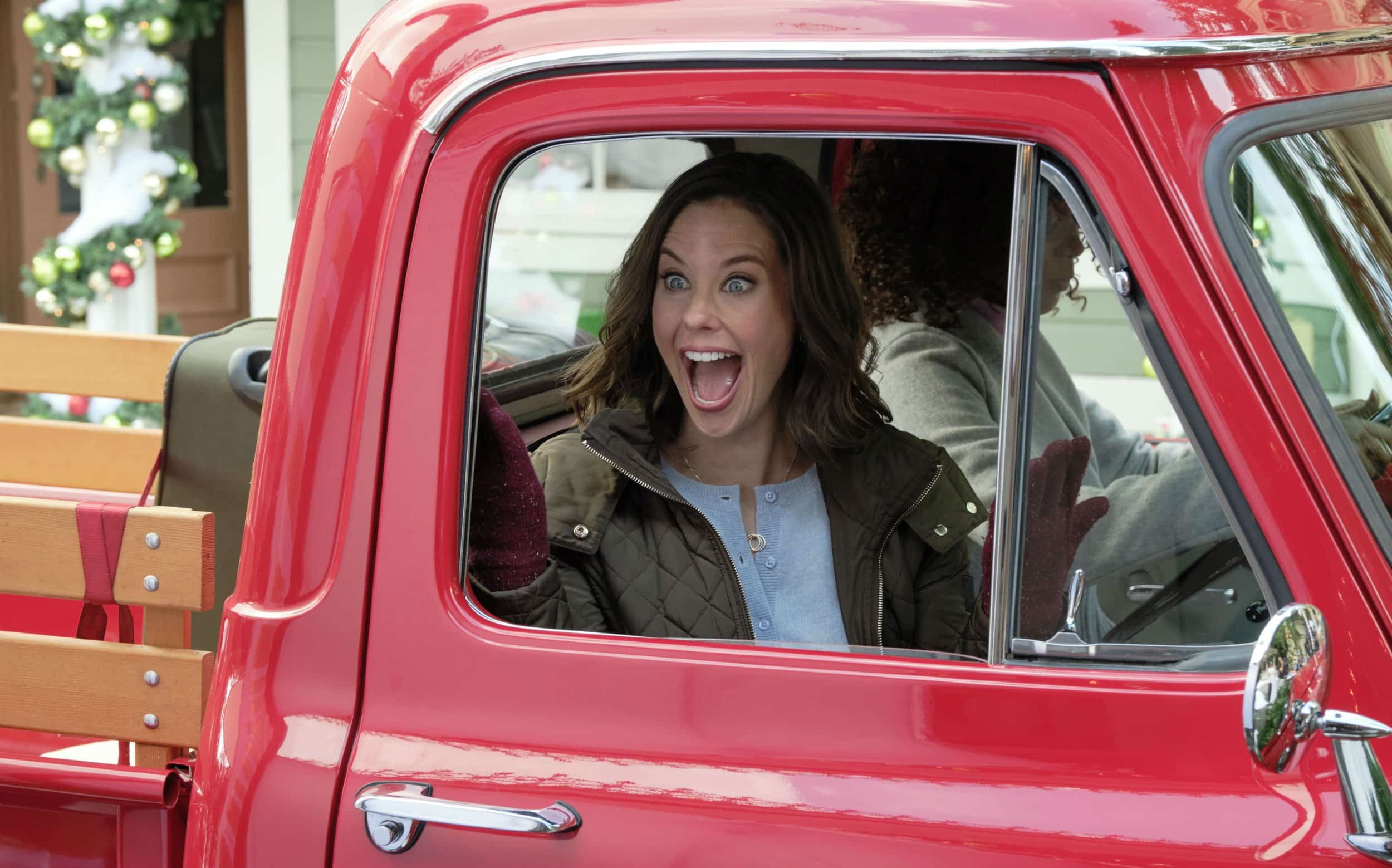 Allie in a red pick-up truck looking excitedly out the open window.