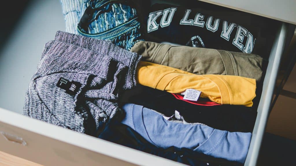 A white, open dresser drawer with miscellaneous t-shirts and sweaters.