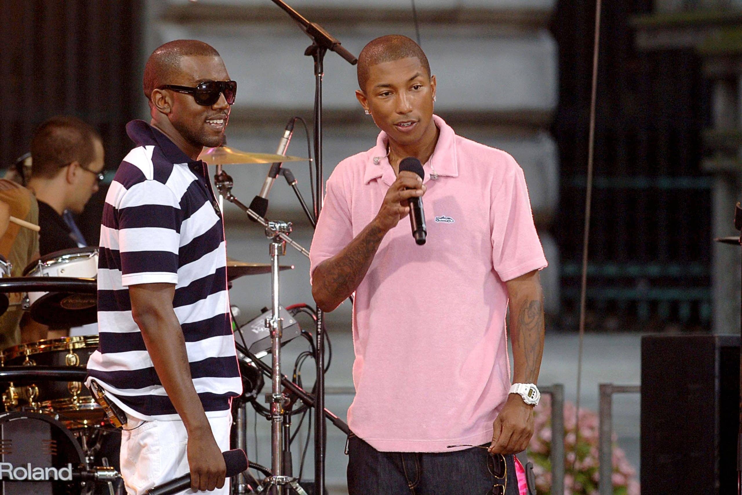 Kanye West standing to the left in a striped black and white collard shirt standing next to Pharrell Williams in a pink collard shirt
