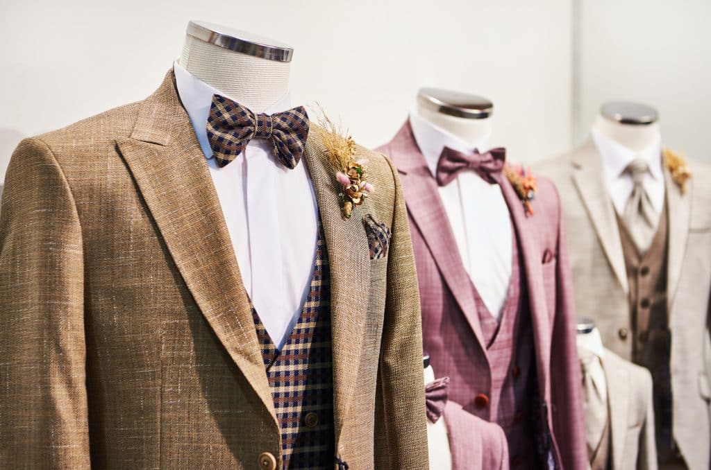Tailored suits sitting on mannequins lined in a row. Suit colors include brown, maroon, and cream.
