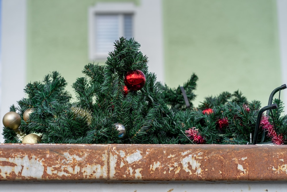 A plastic Christmas tree and ornaments in a dumpster.