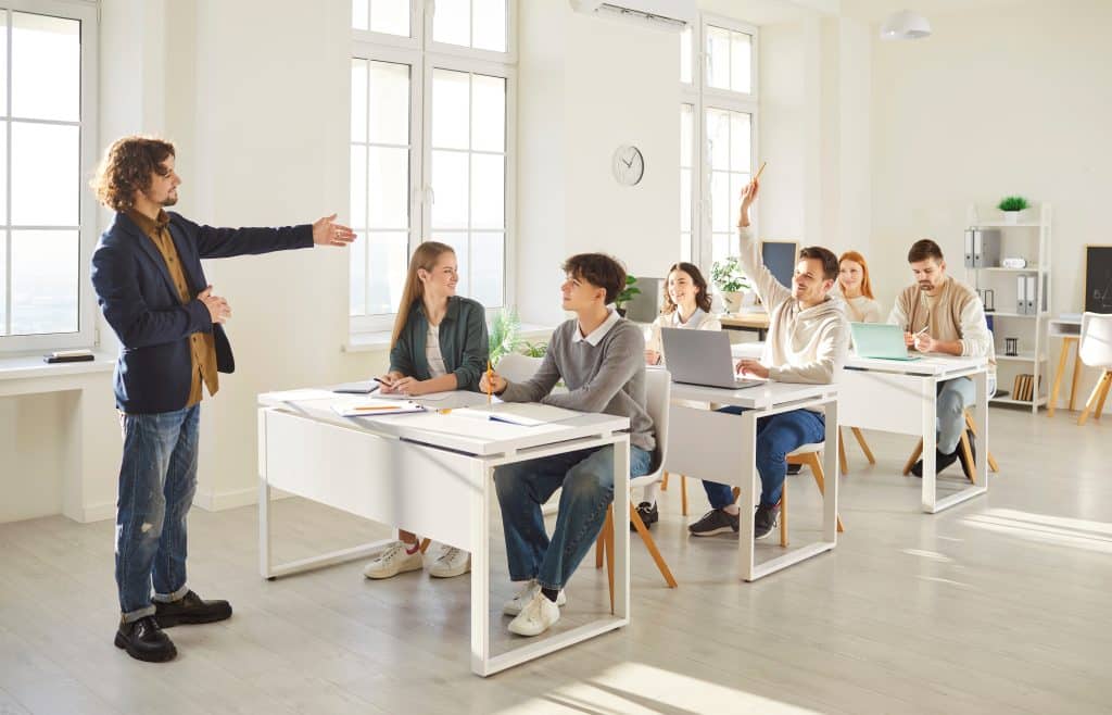 A college classroom with someone putting their hand up.