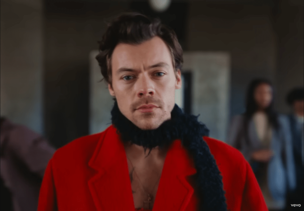 Harry Styles in a red coat and black scarf in the “As It Was” music video
