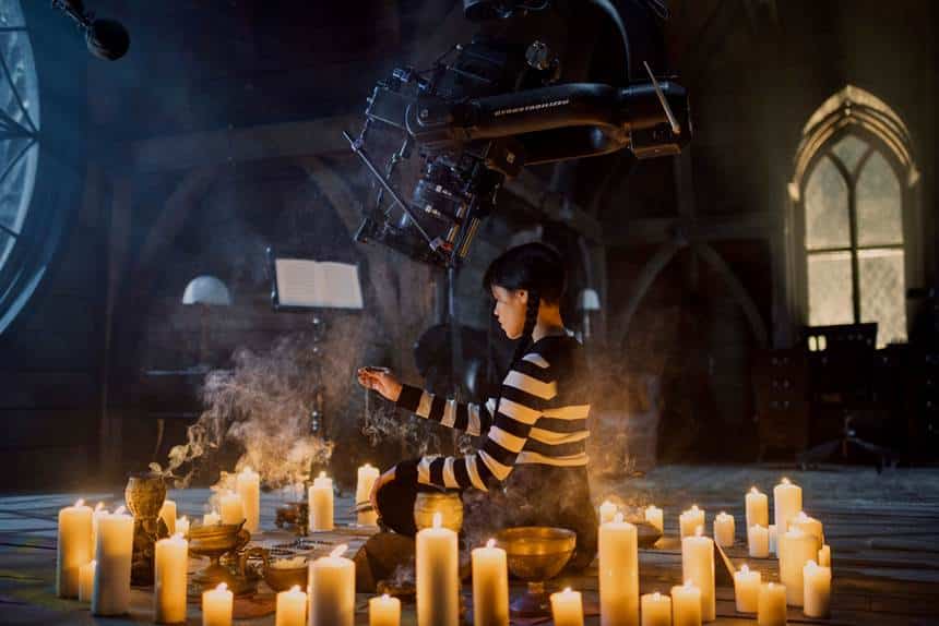 Jenna Ortega as Wednesday Addams, sitting in the middle of a circle of candles