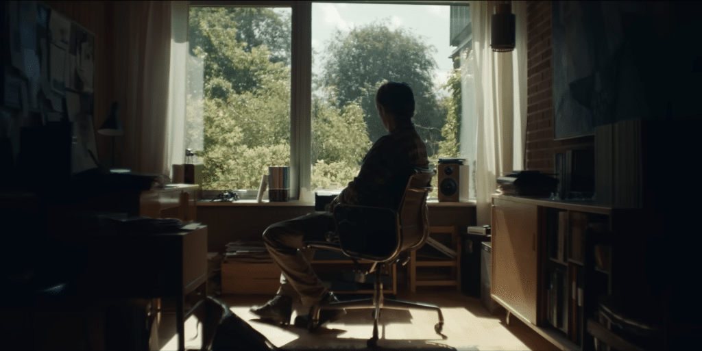Mads Mikkelsen as his character Martin in Danish film Another Round sitting in an arm chair looking out of a window.