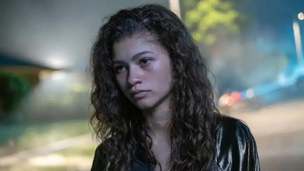 Zendaya as teenager Rue Bennett, who is seen to be standing in a dark street.