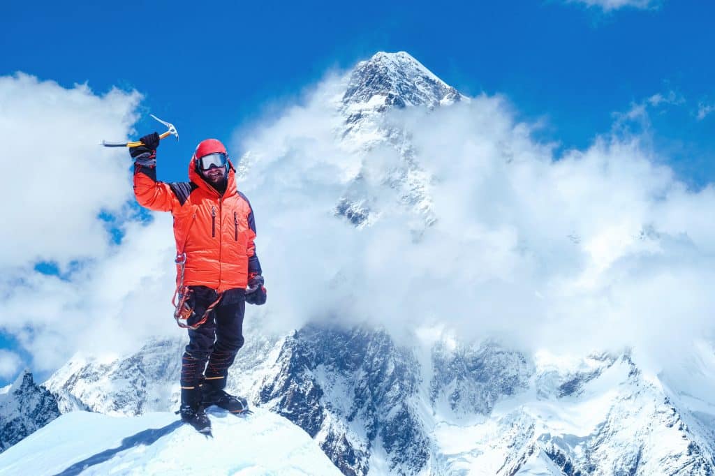 Hiker on the peak of a snowy mountain. Behind him, in the distance, is an even bigger snowy mountain