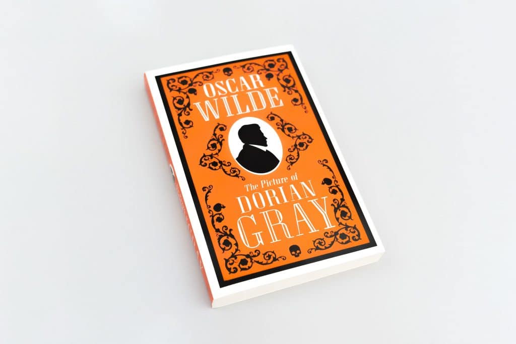A copy of Oscar Wilde's The Picture of Dorian Gray is shown with an orange cover and a black outline of a man in the middle.