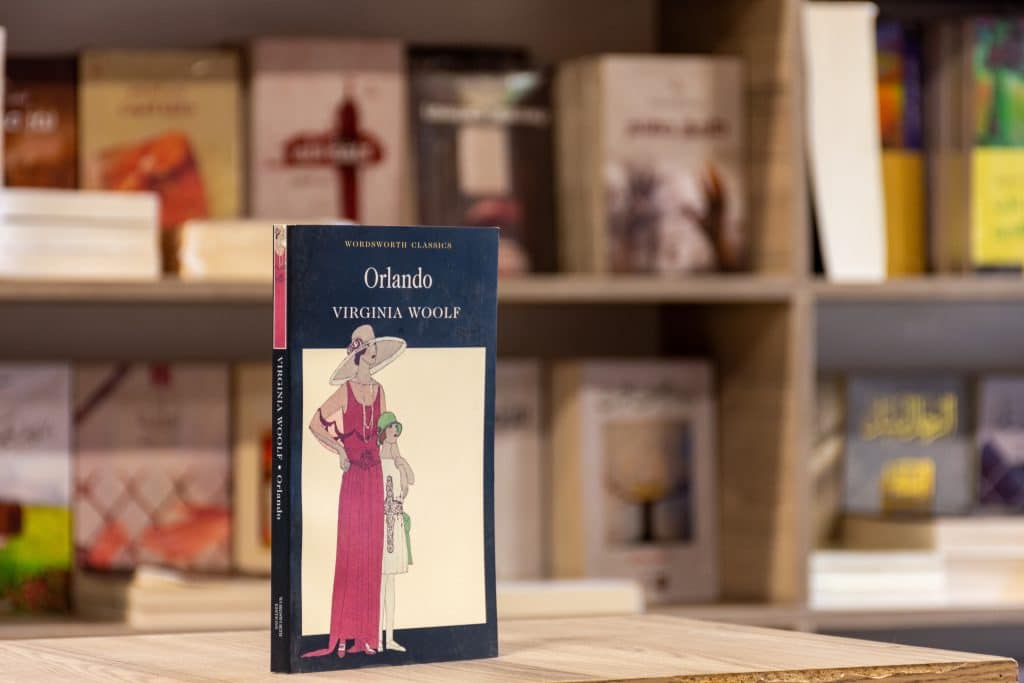 The queer novel Orlando by Virginia Woolf stands up on a table. The cover depicts a woman in a long dress, and a hat.