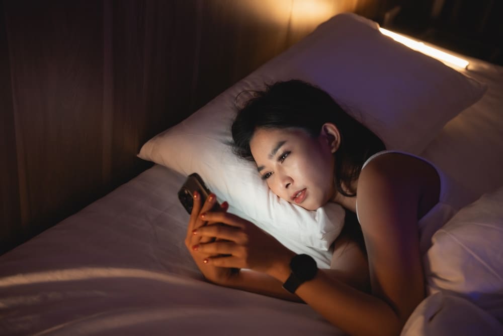 Person laying in bed, in the dark, looking at their phone.